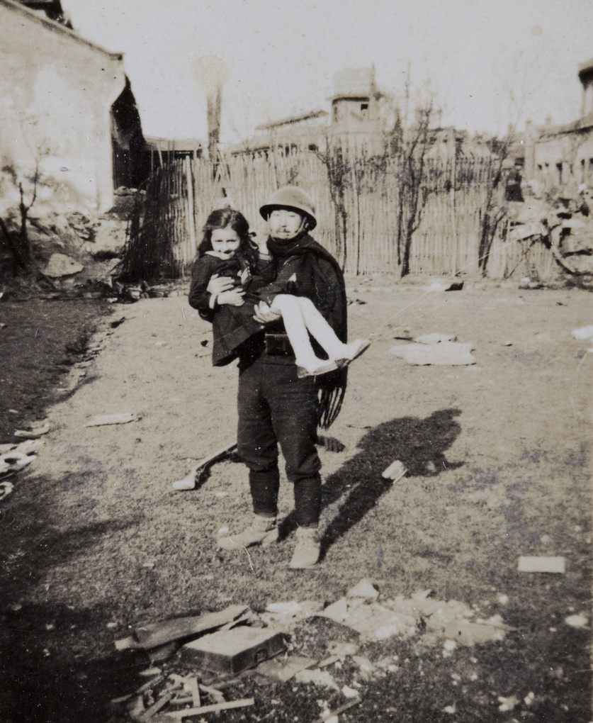 Japanese soldier posing carrying a girl in war damaged area, Shanghai, 1932