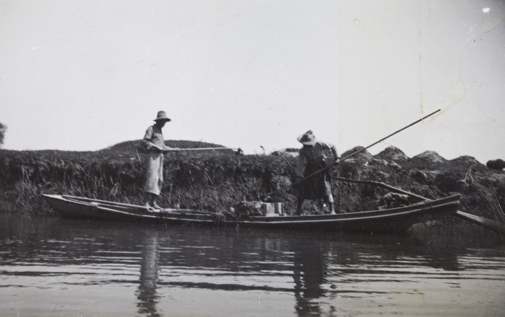 Two men working in a boat on a river near grave mounds