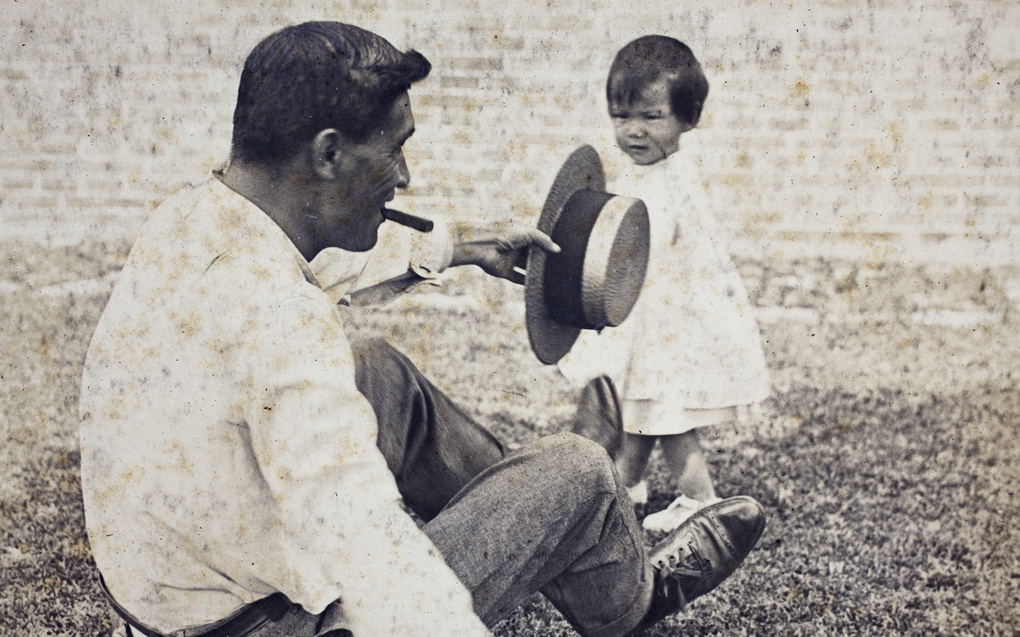 William Hutchinson holding a straw boater hat and sitting on the garden lawn, with his granddaughter, Bea, 35 Tongshan Road, Hongkou, Shanghai