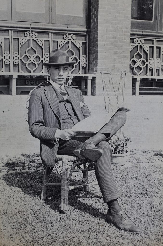 Bill Hutchinson wearing a pin-stripe suit and reading a newspaper in the garden, 35 Tongshan Road, Hongkou, Shanghai