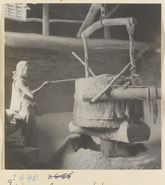 Worker grinding wood into meal using steam-driven mill at incense factory west of Ts'a-ho Village [sic] in the Lost Tribe country