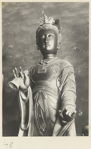 Detail showing the head and torso of a temple statue holding a bell at Xi yu si