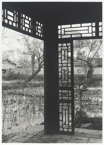 Porch column and latticework at the Old Wu Garden with pond and buildings with ornamental windows in the background