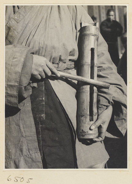 Young Daoist priest playing a bamboo slit drum to attract a crowd