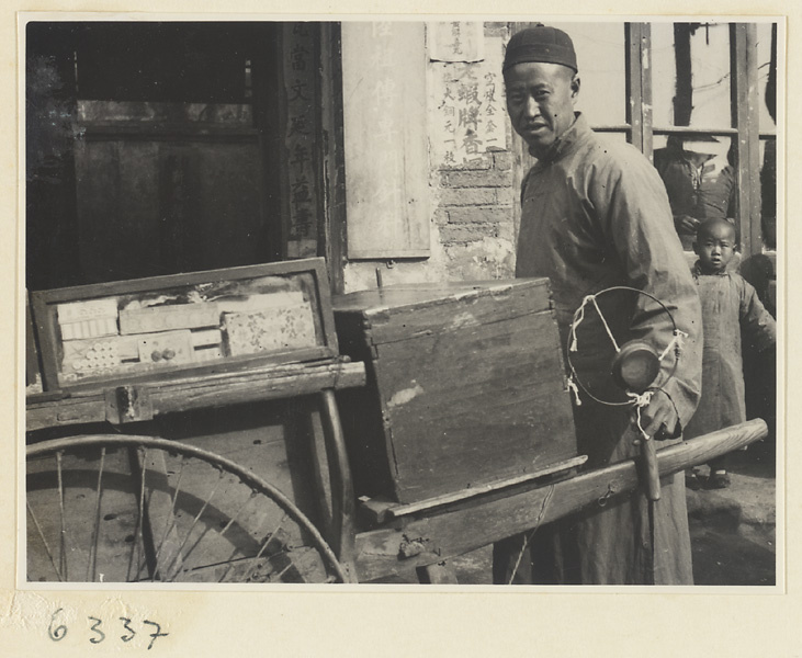 Vendor of sewing supplies pushing his cart and holding a gong called a yun luo or ling zi
