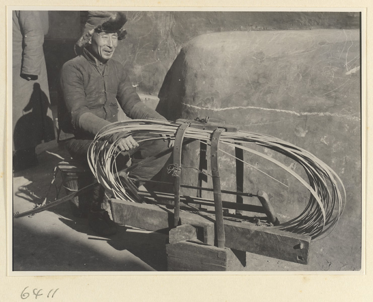 Mat mender seated next to box of tools and reeds