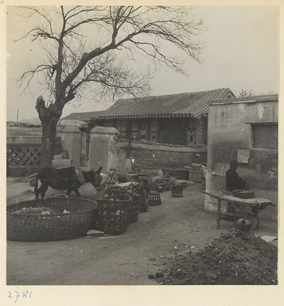 Courtyard of a paper-making shop with donkey harnessed to a grindstone, baskets of paper scraps, and boy hanging paper on a wall to dry