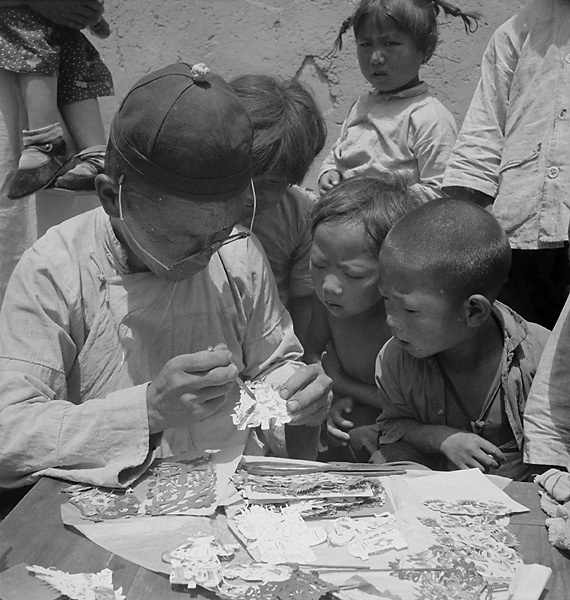 Children watching a man painting paper-cuts