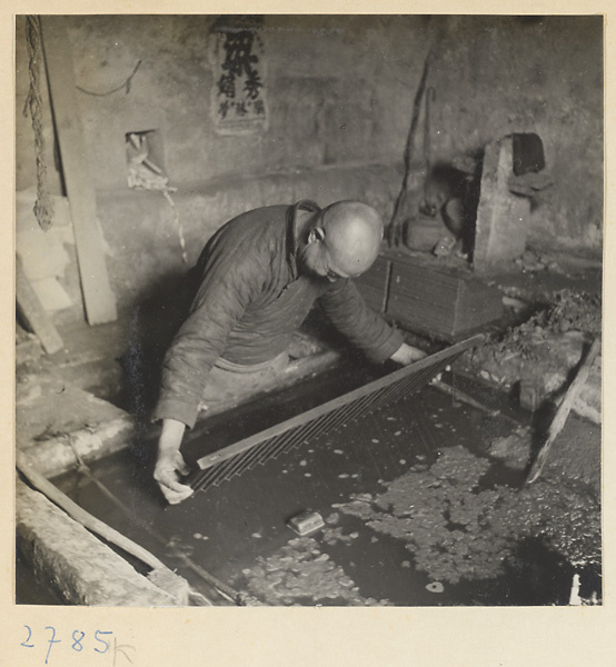 Man placing a screen in a vat of paper pulp in a paper-making shop