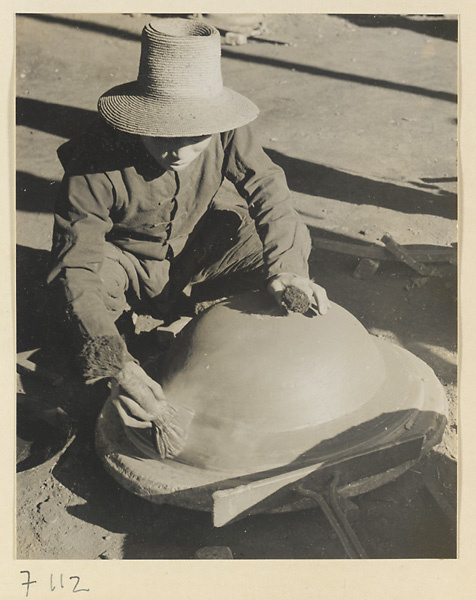Man working on an iron cooking pot with a brush at a foundry near Mentougou Qu