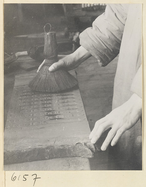 Monk inking a printing block for a new edition of a sutra in the printing room of a Buddhist temple