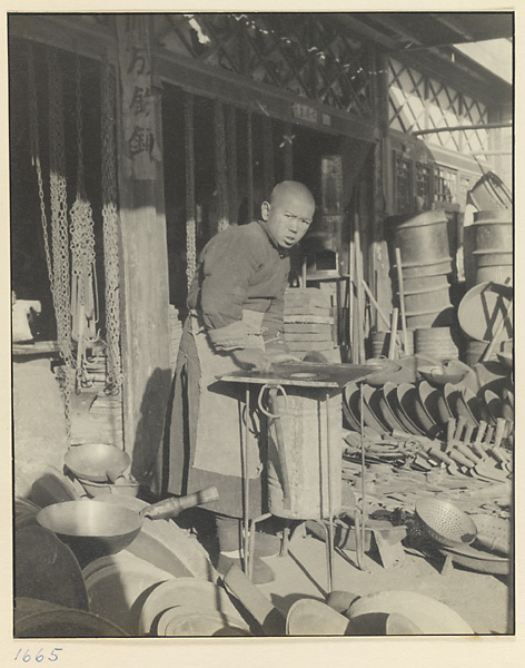 Boy standing next to a portable stove in front of a shop selling metal household goods