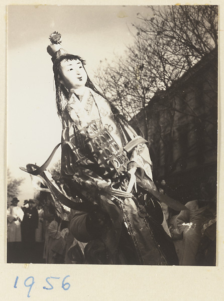 Member of a funeral procession carrying a paper figure of a woman holding a yun luo