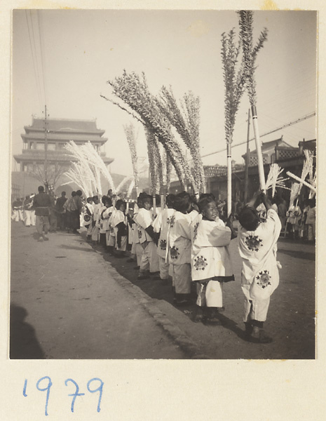 Boys near a city gate holding paper snow willows for a funeral procession