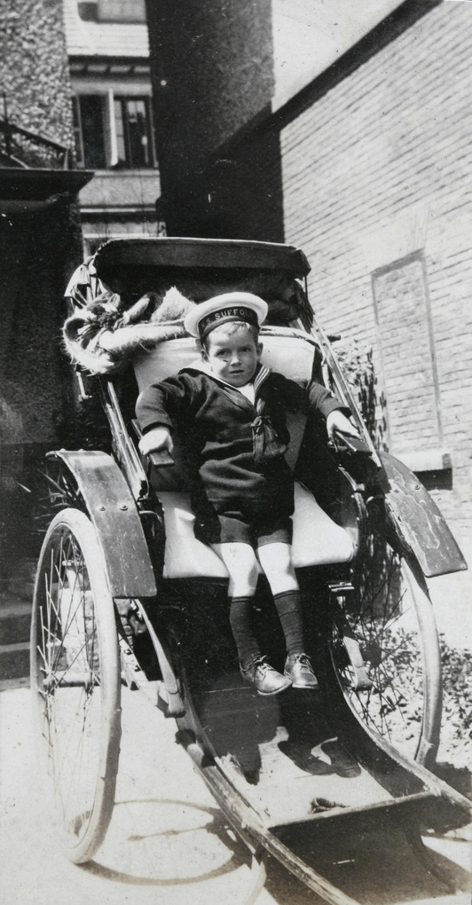 Boy dressed in sailor suit (HMS Suffolk), in a rickshaw