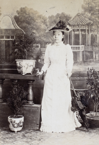 Studio portrait of a Chinese woman holding an umbrella in Western style hat and clothing