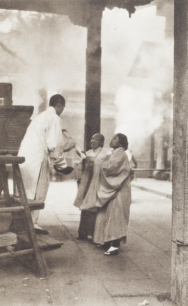Women passing sticks of incense to a Buddhist priest at a temple brazier