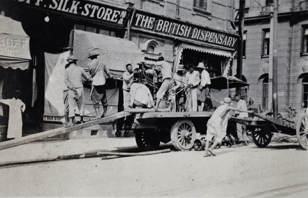Unloading heavy machinery from a steam-powered wagon outside The British Dispensary chemists, North Soochow Road,Shanghai