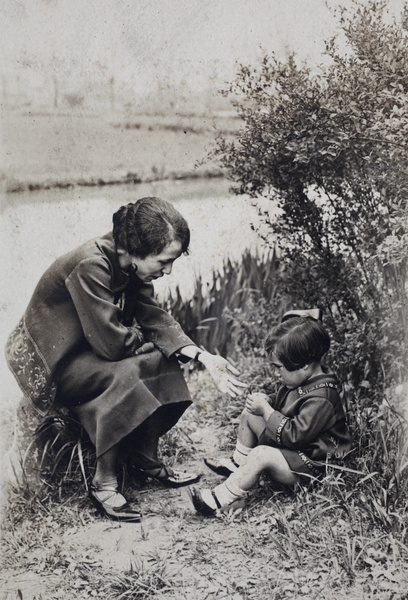 Unidentified woman and daughter sitting near a path beside a river, Shanghai