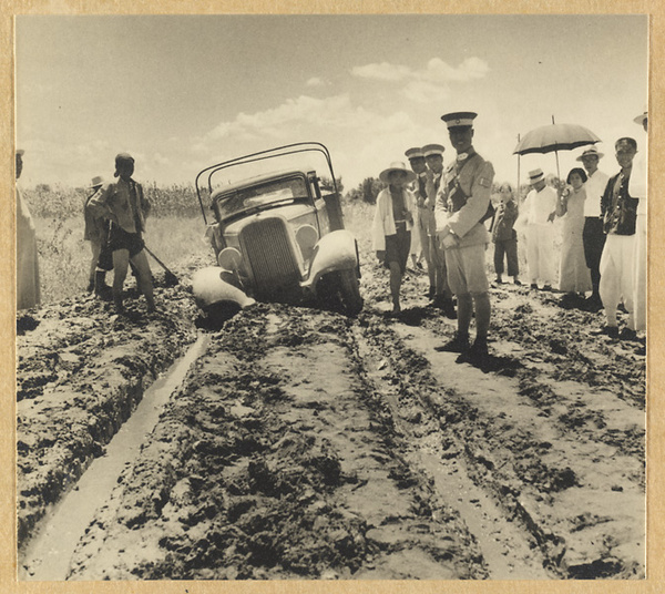 Passengers and Japanese soldiers standing next to truck stuck in the mud on the road from Beijing to Chengde