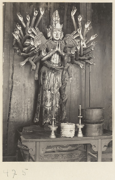 Temple interior showing altar with a statue of a multi-armed, multi-headed Bodhisattva, ritual objects, and staffs at Fa yuan si