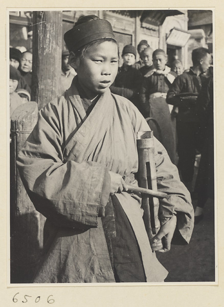Young Daoist priest playing a bamboo slit drum to attract a crowd