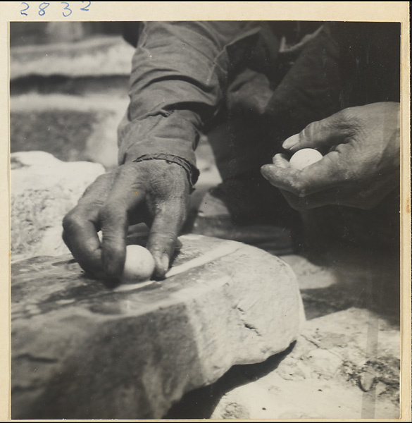 Man smoothing a piece of marble into a ball using a stone drain pipe at Tan zhe si