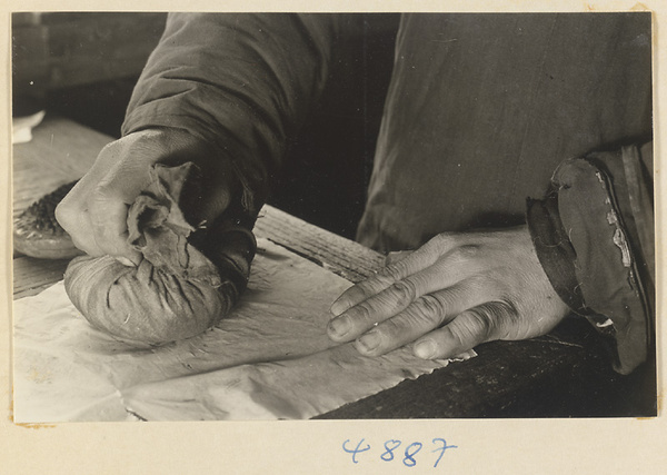 Man impressing cloth or paper onto a sooted metal sheet with a cloth bundle in a workshop that makes iron pictures