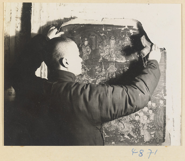 Man in a scroll-mounting shop using a brush to attach a rebacked scroll painting to a drying board called a zhuang ban