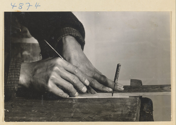 Man in a scroll-mounting shop cutting paper strips with a steel paper knife