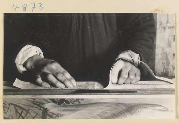 Interior of a scroll-mounting shop showing a man working on the edge of a scroll painting