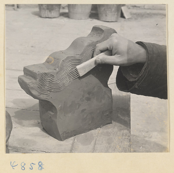 Man adding texture to a ceramic roof ornament at a tile and brick factory near Mentougou Qu