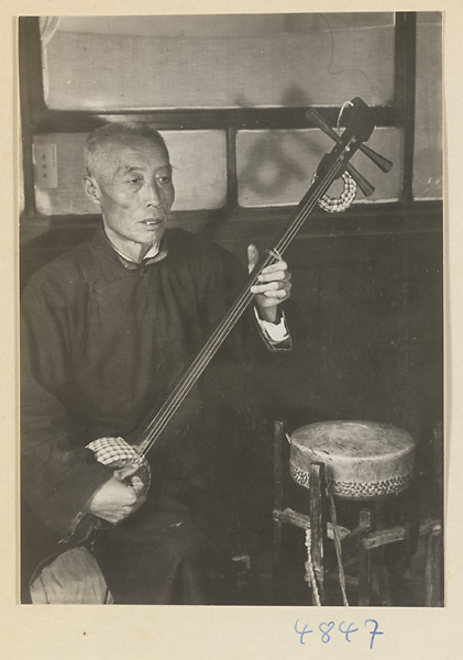 Musician with stringed instrument and drum accompanying a shadow-puppet performance