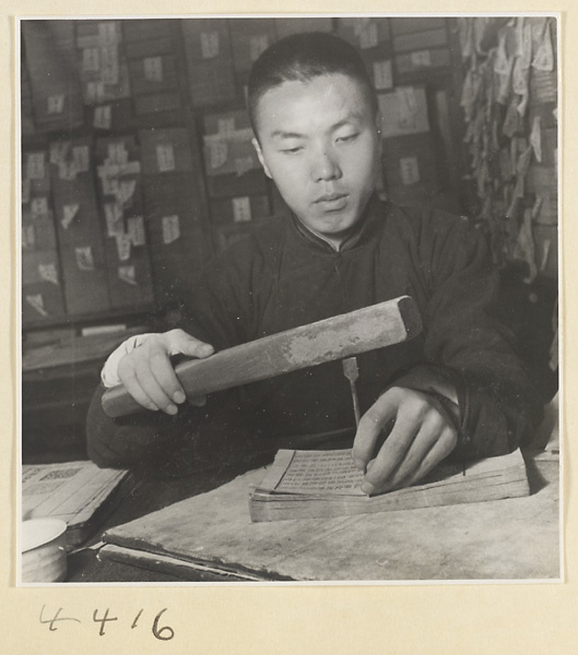 Man pounding a brass awl through the fascicle of a book with a wooden club prior to sewing the binding