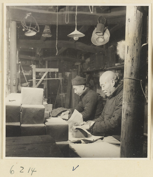 Tobacco shop interior showing men wrapping blocks of pressed tobacco