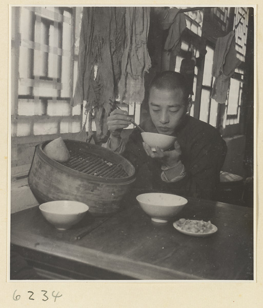 Interior of a scroll-mounting shop showing a man eating