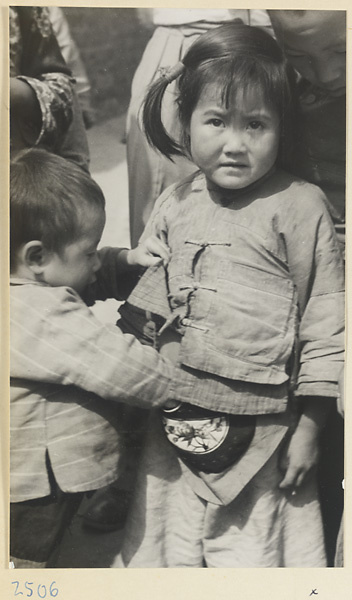 Boy reaching into an embroidered purse worn by a girl in a village on the Shandong coast