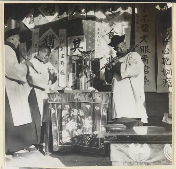 Musicians playing next to hanging elegaic scrolls during a funeral