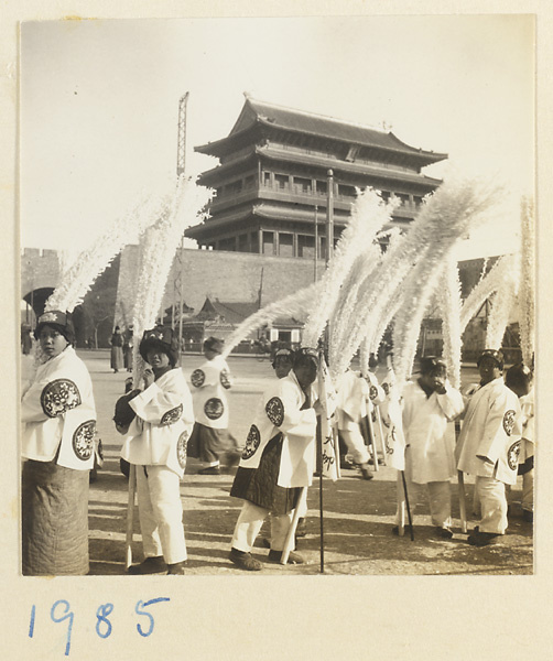 Members of a funeral procession holding paper snow willows near city gate