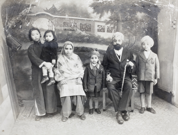 Sikh family group, with amah, in a photographer's studio, Shanghai