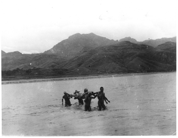A stretcher party carrying a man across a river on a stretcher