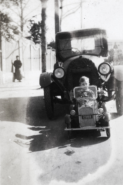 A boy in a pedal car in front of a car