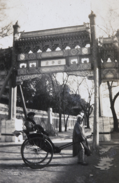 A rickshaw puller and passenger in front of a pailou