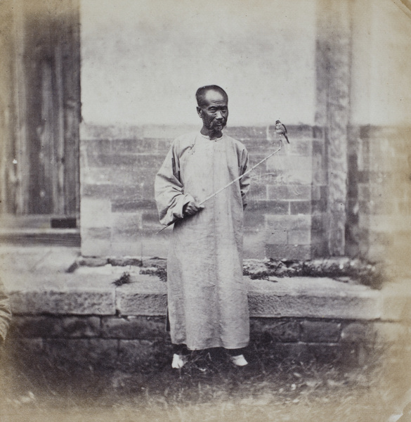 A man with a pet bird tied to a bamboo stick