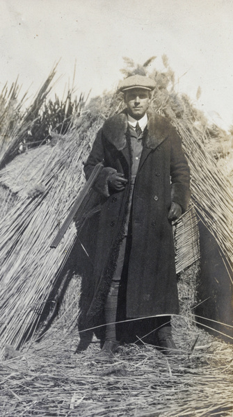 A duck hunter beside a reed structure