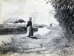 Man beside river with bridge and thatched boat shelter