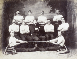 Group photo of British policemen with two men posing as playing tug of war in front, Hong Kong