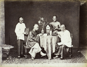 Studio photograph of four men writing, smoking opium and posing with abacus around the table, Hong Kong