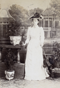 Studio portrait of a Chinese woman holding an umbrella in Western style hat and clothing