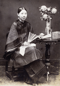 Studio photo of a Chinese woman sitting and posing with a fan and a book